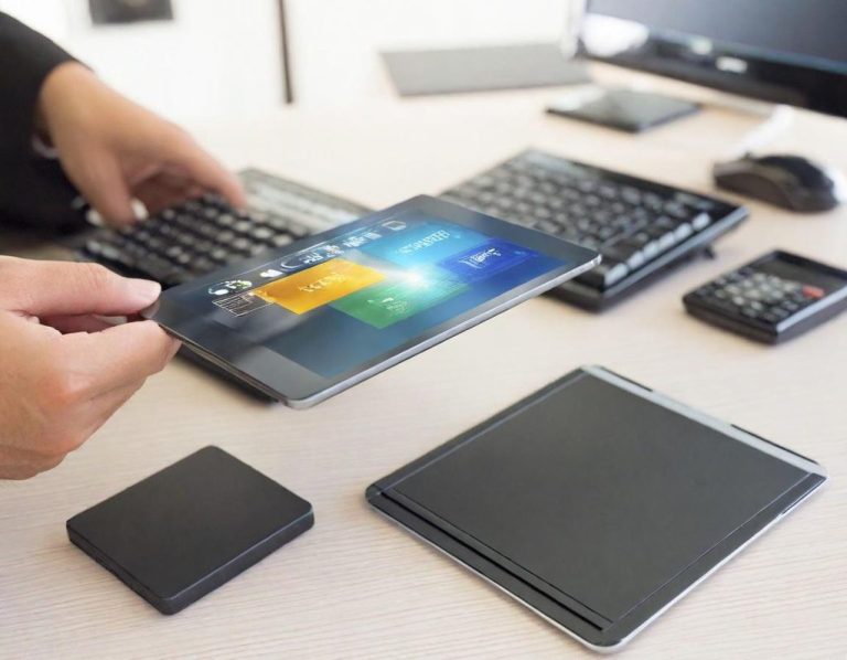 Eine Hand hält ein Tablet über einem Schreibtisch mit Tastatur und Trackpad.